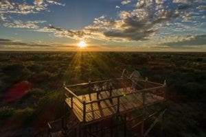 Wooden viewing deck with two people overlooking the Kalahari Desert at sunset.
